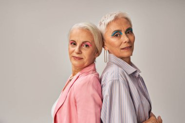Gri arka planda arka arkaya duran zarif mavi ve pembe elbiseli çekici yaşlı kadınlar.