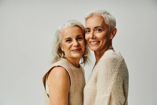 modern senior female friends in pastel clothes smiling at camera on grey, happy and stylish aging