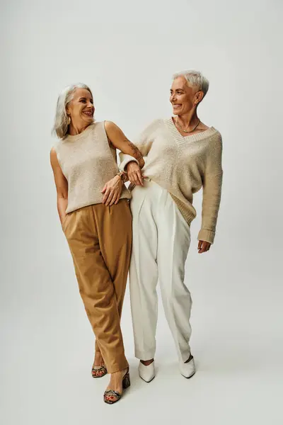 stock image full length of joyful and stylish female friends looking at each other on grey, senior fashion
