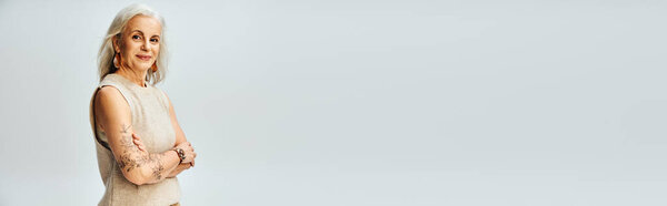 trendy senior model with silver hair, tattoo and folded arms looking at camera on grey, banner