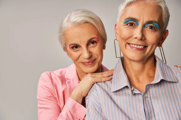 portrait of fashionable senior models with silver hair and makeup smiling at camera on grey