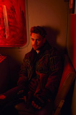 Kirli metro vagonunda kırmızı ışıkta oturan, kıyamet sonrası hayatta kalan düşünceli bir adam.