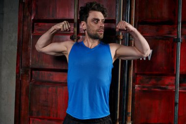 Sportif traşsız adam konteynırın yanında güç gösteriyor ve caddeye bakıyor.