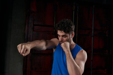 concentrated unshaven man working out and boxing in darkness on city street clipart