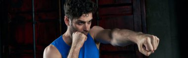 confident unshaven man in blue tank top training and boxing on city street at night clipart