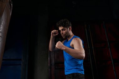 confident unshaven man in sportswear working out with punching bag on street at night clipart