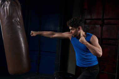 unshaven sportive man boxing punching bag in darkness on urban street, outdoor workout clipart