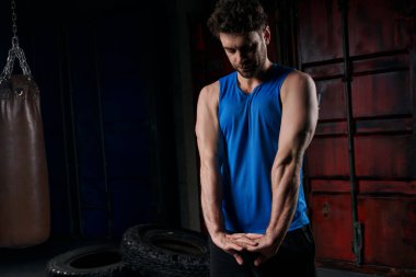 Mavi kolsuz tişörtlü atletik adam geceleri şehir sokağında egzersiz yapıyor ve kollarını esnetiyor.