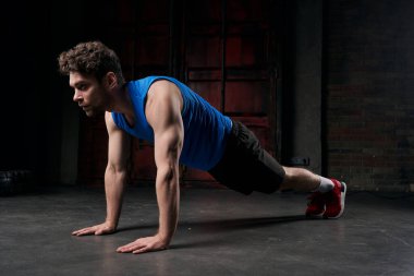 Karanlık bir şehirde gece boyunca spor kıyafetleri içinde tahta pozlar veren güçlü bir adam.