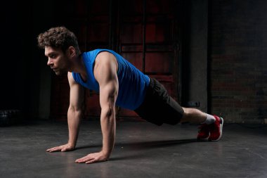full length of vigorous man in sportswear training in plank pose in dark city at night clipart