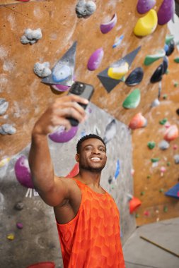 Genç Afrikalı Amerikalı adamın kaya tırmanışı arka planında selfie çekerken dikey görüntüsü.