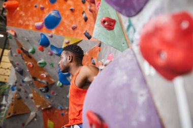 good looking african american male model posing next to rock climbing wall and looking away clipart
