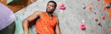Sportif Afrikalı Amerikalı adam kaya tırmanışı duvarının yanında duruyor ve başka yere bakıyor, kayalar, afişler...