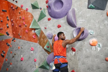 İyi görünümlü Afro-Amerikan adam poz veriyor ve kaya duvarına tırmanıyor Alp koşum takımı, spor