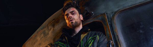 Хмурый человек с небритым поцарапанным лицом, смотрящий в камеру в темном метро после катастрофы, баннер