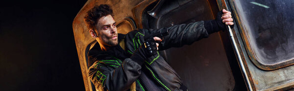 небритый человек, нацеленный с пистолетом в темноте метро после катастрофы, опасность и выживание, знамя