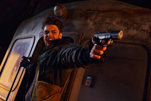 кричащий человек, стреляющий из пистолета в темноте заброшенного постапокалиптического метро, опасности и отчаяния