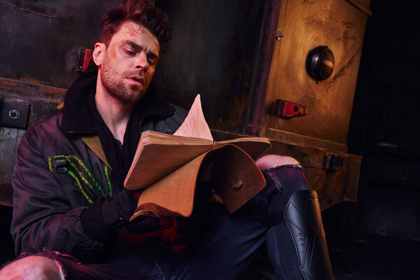 Небритый раненый сидит в заброшенном постапокалиптическом метро и читает воспоминания в дневнике