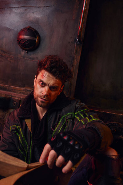 devastated unshaven man in worn clothes sitting with diary near rusty carriage in abandoned subway