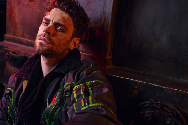 game character with scratched unshaven face looking at camera in darkness of abandoned subway