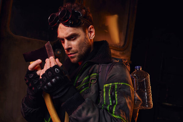 man with military goggles checking sharpness of axe in dangerous environment of abandoned subway