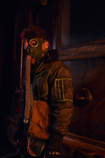 man in dirty jacket and gas mask near rusty subway carriage in abandoned underground tunnel
