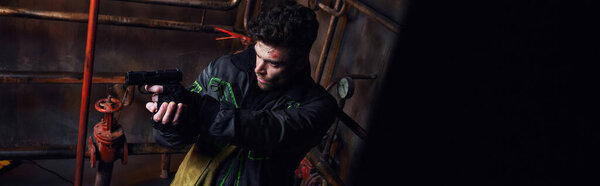 небритый мужчина в изношенной одежде, нацеленный с оружием в подполье после катастрофы, высокий угол обзора, баннер