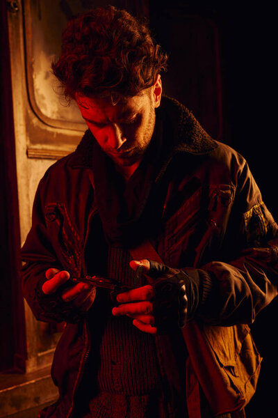man in black jacket looking at pressure gauge in carriage of post-apocalyptic subway with red light
