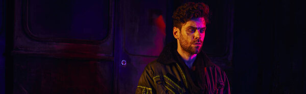 вдумчивый небритый мужчина в черной куртке в темном постапокалиптическом метро с красным светом, баннер