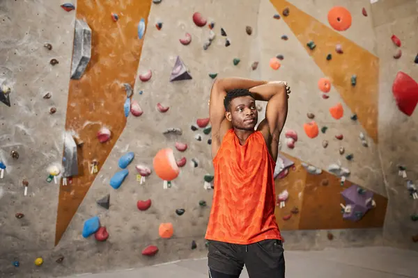 stock image sporty african american man with hands behind head looking away with climbing wall on backdrop