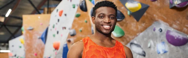 joyful african american man smiling cheerfully at camera with rock climbing wall backdrop, banner