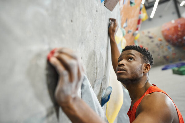 good looking young african american man climbing up bouldering wall and looking up, sportsman