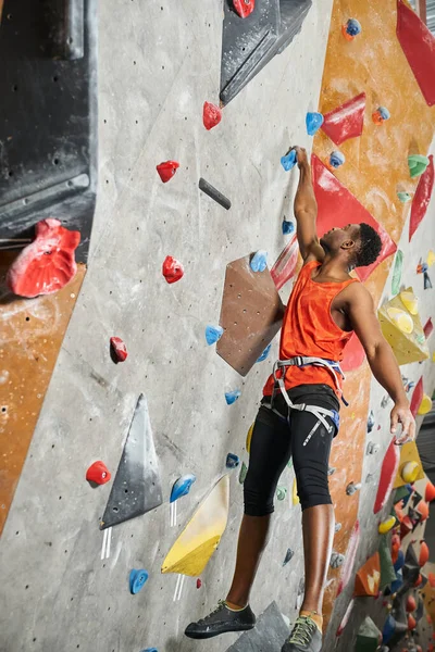 stock image athletic african american man hanging on his fingertips on climbing rock wall, vertical shot