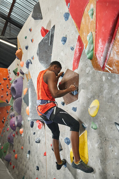 vertical shot of muscular african american man climbing up bouldering wall and looking down