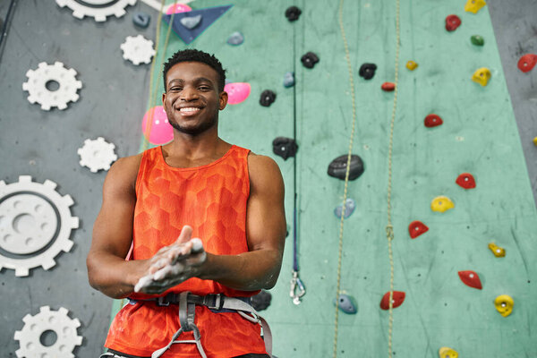 cheerful african american man using talc powder before climbing up wall smiling at camera joyfully