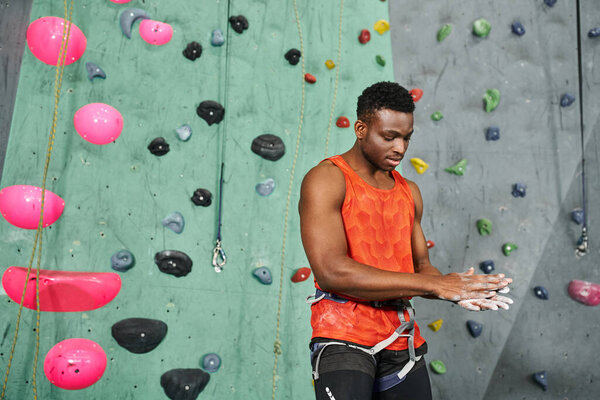good looking african american male model in orange shirt with alpine harness using talc powder