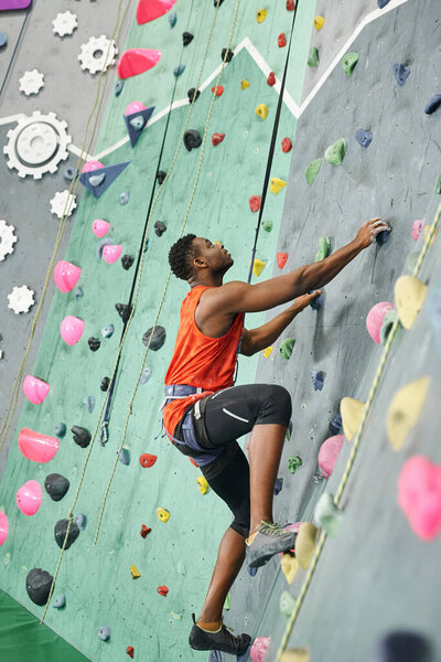 vertical shot of athletic young african american man ascending up rock wall with safety rope