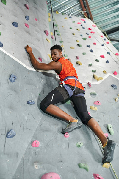 handsome african american man with safety rope and alpine harness climbing and looking down