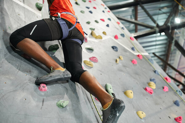 cropped view of strong african american man with alpine harness climbing up bouldering wall