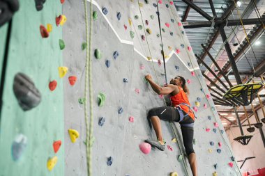 sporty african american man in orange shirt climbing up wall and gripping on boulders, rock wall clipart