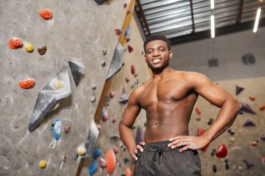 cheerful shirtless african american man posing with his hands on hips and smiling at camera clipart