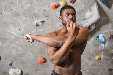 Güçlü, yakışıklı, Afro-Amerikan bir adam üstsüz poz veriyor ve kameranın önünde kollarını açıyor.