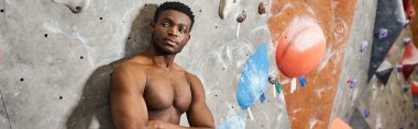 Kollarını göğsünde kavuşturup tişörtsüz poz veren yakışıklı Afro-Amerikan bir adam.