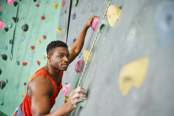 good looking african american man gripping on boulders using safety rope and looking at camera