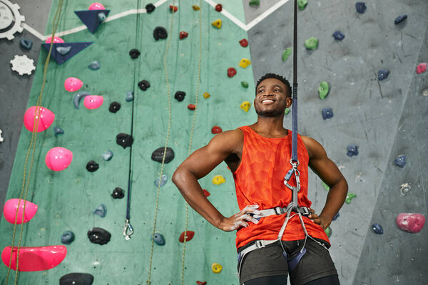 cheerful african american man with his hands on hips posing with safety rope and looking away