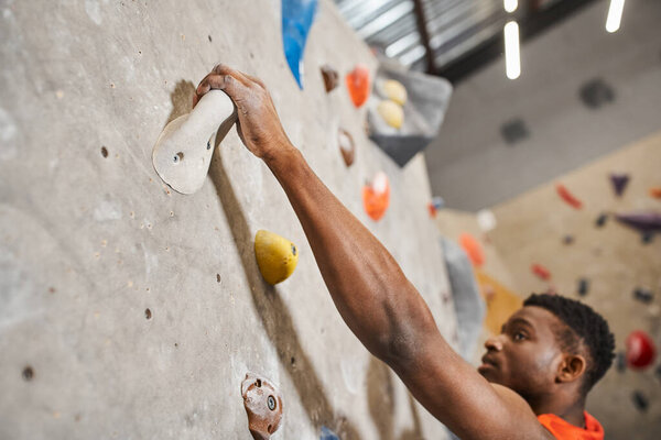close up of handsome african american man gripping on boulders while climbing up rock wall