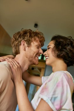 side view of happy interracial couple looking at each other and laughing, having a good time clipart