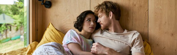 межрасовая пара нежный момент, лежа вместе на кровати и глядя друг на друга, баннер