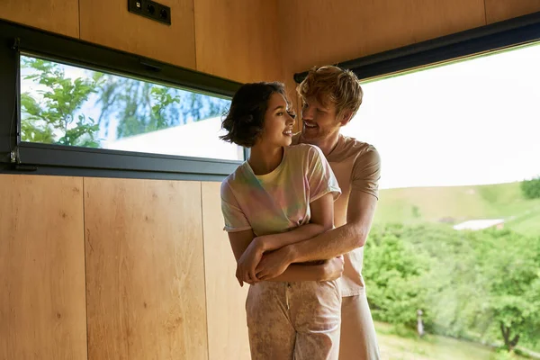 Vreugdevolle Roodharige Man Knuffelen Aziatische Vriendin Naast Venster Met Uitzicht — Stockfoto