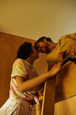 happy asian woman climbing wooden ladder of bunk bed near redhead boyfriend, weekend getaway clipart